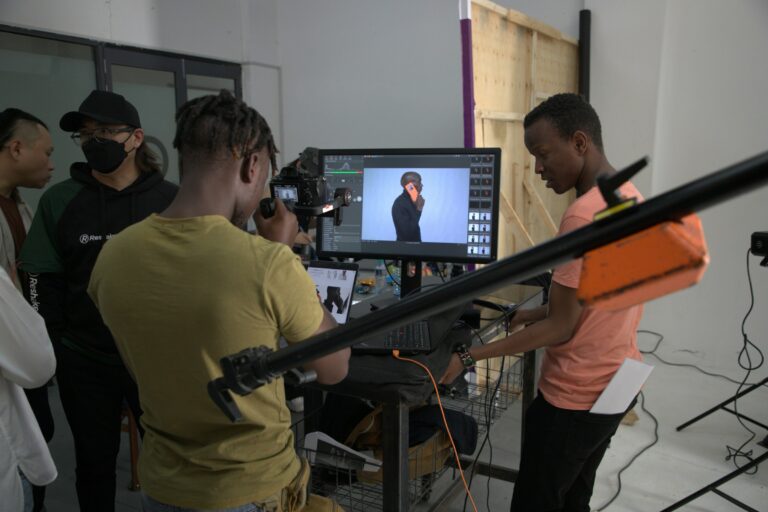 A video crew in a Nairobi studio reviews a shot on a monitor while a camera operator films a subject against a backdrop