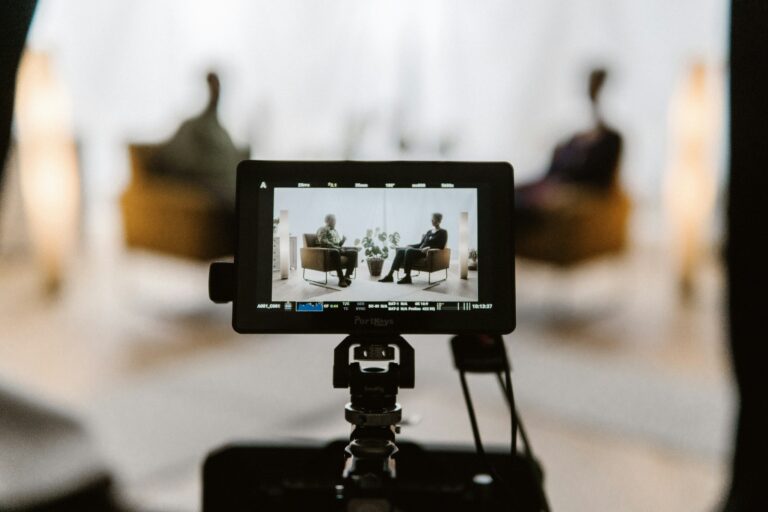 A camera monitor on a tripod framing a seated two-person interview on a video shoot