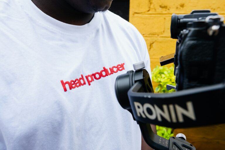 Videographer in a white "head producer" T-shirt holding a camera on a Ronin gimbal stabiliser, Nairobi, Kenya